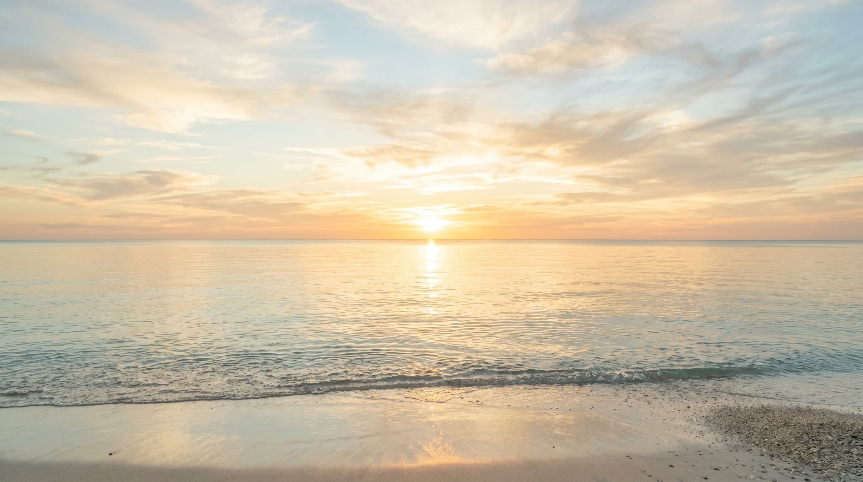 A calm clear sea meeting a luminous sky at sunrise.